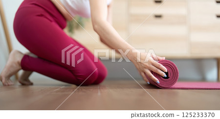 Yoga and Mindful Ending. A woman rolling up her yoga mat after a session of tranquility. 125233370