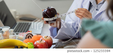 Nutritionist Consultation and Healthy Choices. A nutritionist measures an apple while discussing healthy eating habits with a client. Nutritionist Consultation and Healthy Choices. A nutritionist measures an apple while discussing healthy eating habits with a client. 125233394