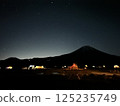 A beautiful night camping scene with a lit tent under the starry sky and the silhouette of Mt. Fuji 125235749