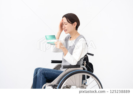 A woman in a wheelchair is depressed when she sees her bankbook 125238889