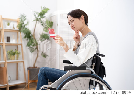 A woman in a wheelchair is depressed when she sees her bankbook 125238909