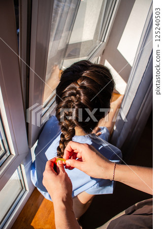 Woman braiding her daughter's hair. Mother and daughter enjoying quiet intimate moment Precise braiding process shown in detail. 125240503