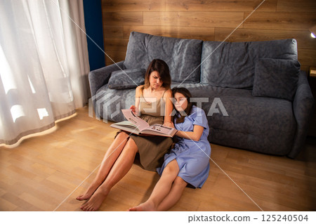 Adult female reading book aloud to preteen girl who seems disinterested in book. Home education concept. Child with limited attention fallen asleep during book reading. Adult female reading book aloud to preteen girl who seems disinterested in book. Home education concept. Child with limited attention fallen asleep during book reading. 125240504