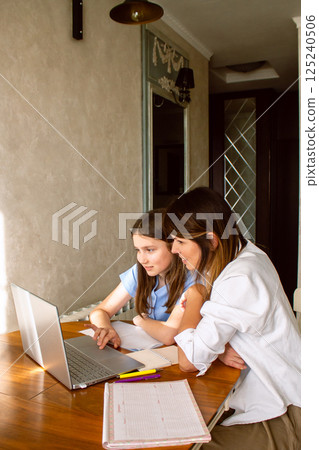 Happy mother with preteen daughter using laptop in home kitchen. Working on school project. Helping with homework using technologies. Happy mother with preteen daughter using laptop in home kitchen. Working on school project. Helping with homework using technologies. 125240506