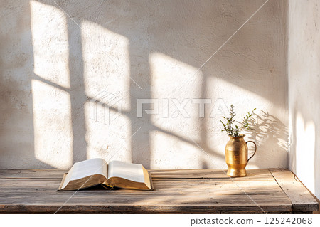 An open book rests on a wooden desk under soft warm light, creating a minimalist yet inviting scene 125242068