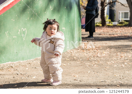 [One-year-old child standing and playing in a park with fallen winter leaves] 125244579