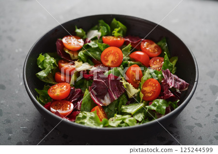 Salad with green and purple leaves and cherry tomatoes in black bowl Salad with green and purple leaves and cherry tomatoes in black bowl 125244599