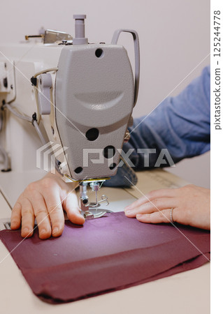 woman sews piece of cloth on sewing machine. industrial metal machine for all fabric tops. woman sews piece of cloth on sewing machine. industrial metal machine for all fabric tops. 125244778