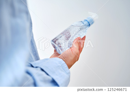 An unrecognizable person in blue clothes holds a bottle of hyaluronic micellar gel for washing. An unrecognizable person in blue clothes holds a bottle of hyaluronic micellar gel for washing. 125246671