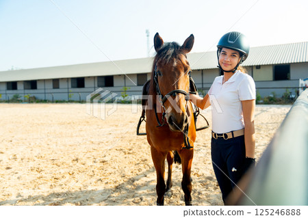 Teen girl stand beside brown horse and look at camera after train or practice for riding in the arena. 125246888