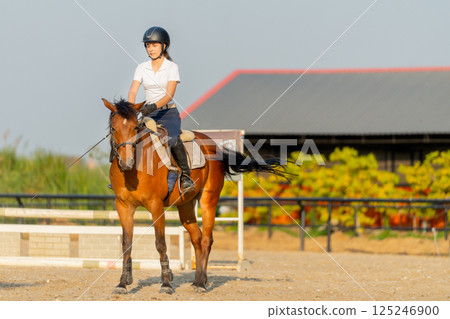Smart teen girl enjoy to ride horse for exercise and train in the horse riding arena. Smart teen girl enjoy to ride horse for exercise and train in the horse riding arena. 125246900