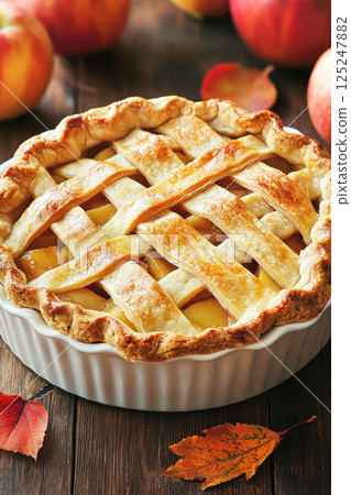 Freshly baked lattice apple pie placed on a rustic wooden surface, surrounded by ripe apples, capturing the warmth of a classic homemade dessert. 125247882