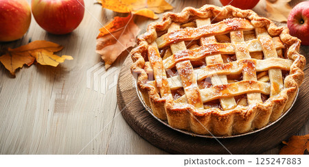Freshly baked lattice apple pie placed on a rustic wooden surface, surrounded by ripe apples, capturing the warmth of a classic homemade dessert. 125247883