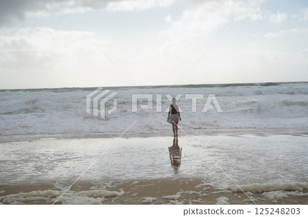 Woman Gazing at Ocean Waves on a Cloudy Day 125248203