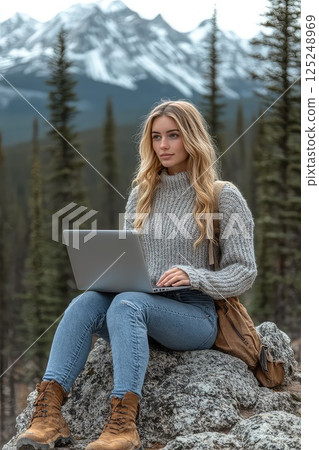 Woman during hike sitting on a rock with a laptop on her lap. Remote work. A young woman balances work and nature, using her laptop on a rock to embrace the freelance lifestyle. 125248969