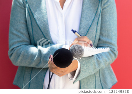 Female journalist at news conference, writing notes, holding microphone 125249828