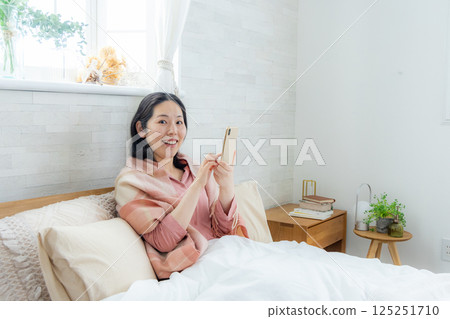 一名婦女在床上的看一個智能手機 125251710