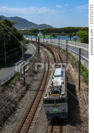 A 150m rail transport train towed by a silver kettle running with Dokai Bay in the background (JR Freight) 125252312