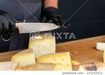 A vendor slices a piece of cheese with a knife at a farmers market 125252412