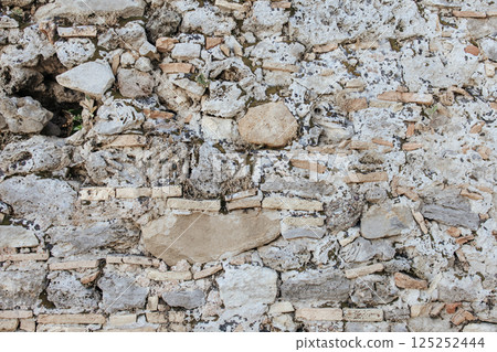 Texture of an old stone wall made of limestone, brick and mortar. Traces of time, cracks, moss and remains of vegetation between the stones are visible. Natural texture of Stone. 125252444