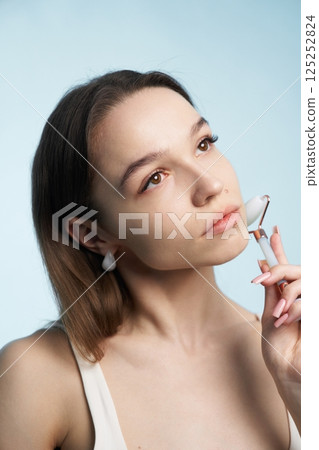 Woman using facial roller while contemplating beauty routine in soft lighting 125252824