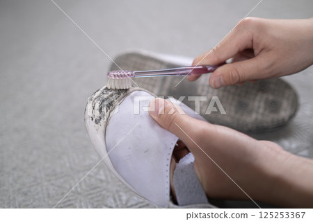 A child's hand trying to remove dirt from his school shoes with a toothbrush 125253367