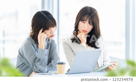 Two women/businesswomen thinking while using a laptop Two women/businesswomen thinking while using a laptop 125254979