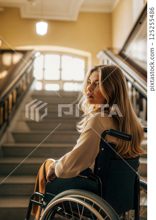 Young Woman in Wheelchair Sits on Staircase in a Beautifully Lit Building During the Day Young Woman in Wheelchair Sits on Staircase in a Beautifully Lit Building During the Day 125255486