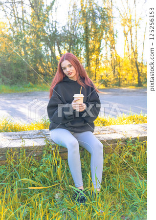 Redhead girl drinking in the park 125256153