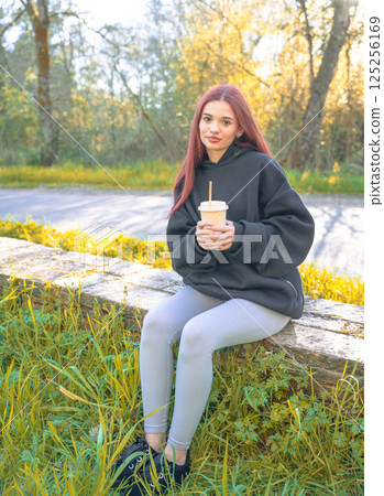 Redhead girl drinking in the park Redhead girl drinking in the park 125256169