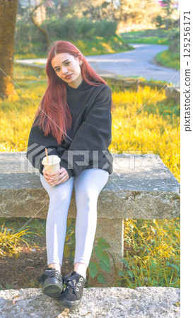 Redhead girl drinking in the park 125256171