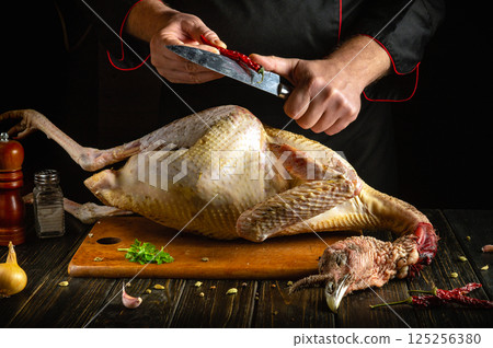 A person is skillfully chopping herbs and spices above a whole turkey on a wooden board. The scene captures the essence of meal preparation in a warm kitchen A person is skillfully chopping herbs and spices above a whole turkey on a wooden board. The scene captures the essence of meal preparation in a warm kitchen 125256380