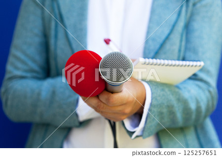 Female journalist at news conference, writing notes, holding microphone Female journalist at news conference, writing notes, holding microphone 125257651