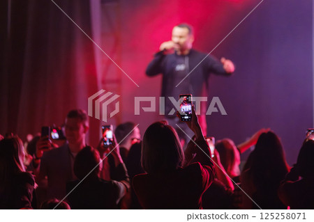 Excited crowd capturing live singer performing on stage with vibrant red lights Excited crowd capturing live singer performing on stage with vibrant red lights 125258071