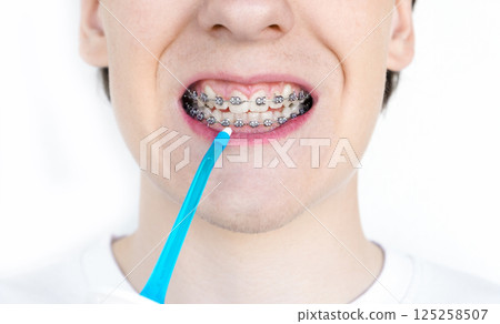 A young unrecognizable man with braces cleaning his teeth with oral irrigator. 125258507