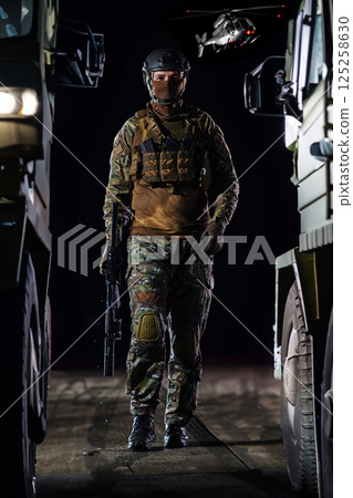 A soldier marching through the dark of night, accompanied by two military trucks, as he embarks on a perilous military mission, embodying the unwavering determination, teamwork, and preparedness 125258630