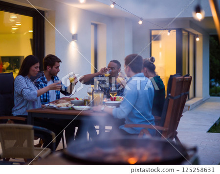 A group of young diverse people having dinner on the terrace of a modern house in the evening. Fun for friends and family. Celebration of holidays, weddings with barbecue 125258631