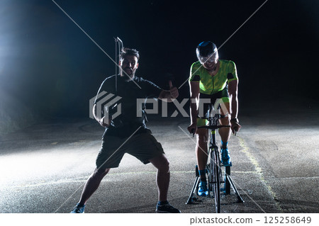 Behind the scenes. Professional videographer on a night shoot with a triathlete riding a bicycle for video recording purposes 125258649