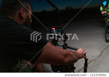 A videographer recording a triathlete riding his bike preparing for an upcoming marathon.Athlete's physical endurance and the dedication required to succeed in the sport. A videographer recording a triathlete riding his bike preparing for an upcoming marathon.Athlete's physical endurance and the dedication required to succeed in the sport. 125258692