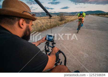 A videographer recording a triathlete riding his bike preparing for an upcoming marathon.Athlete's physical endurance and the dedication required to succeed in the sport. 125258694