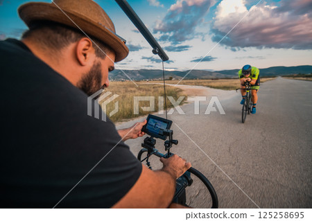 A videographer recording a triathlete riding his bike preparing for an upcoming marathon.Athlete's physical endurance and the dedication required to succeed in the sport. 125258695