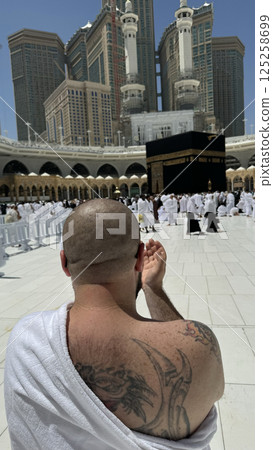 Former Sinner man who converted to Islam, with a large tattoo on his back and arm, praying with devotion in Makkah while gazing at the sacred Kaaba, embracing his new faith with deep spiritual 125258699