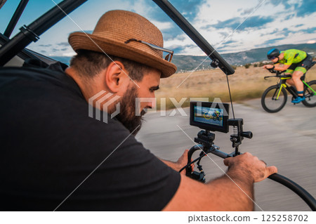 A videographer recording a triathlete riding his bike preparing for an upcoming marathon.Athlete's physical endurance and the dedication required to succeed in the sport. 125258702