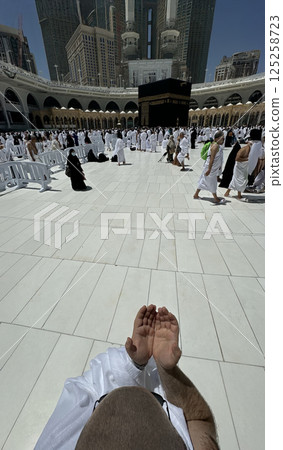 A bald man poses for a photo in front of the Kaaba at noon after performing Umrah at Masjid al-Haram, Mecca. A sacred Islamic pilgrimage in the heart of the holy mosque under the bright sunlight. A bald man poses for a photo in front of the Kaaba at noon after performing Umrah at Masjid al-Haram, Mecca. A sacred Islamic pilgrimage in the heart of the holy mosque under the bright sunlight. 125258723