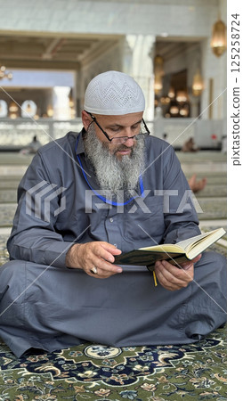 Mecca, Saudi Arabia - May 2, 2024: Young man, Hajj and Umrah pilgrim sitting and reading Quran in Masjidil Haram, Great Mosque in Makkah, Saudi Arabia. Hajj 2024. Mecca, Saudi Arabia - May 2, 2024: Young man, Hajj and Umrah pilgrim sitting and reading Quran in Masjidil Haram, Great Mosque in Makkah, Saudi Arabia. Hajj 2024. 125258724