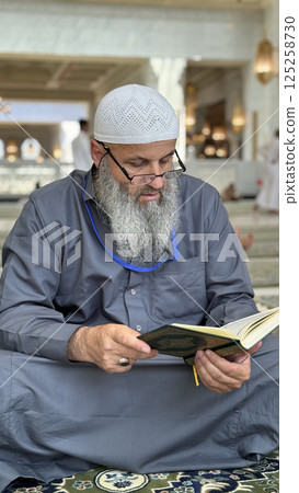 Mecca, Saudi Arabia - May 2, 2024: Young man, Hajj and Umrah pilgrim sitting and reading Quran in Masjidil Haram, Great Mosque in Makkah, Saudi Arabia. Hajj 2024. 125258730