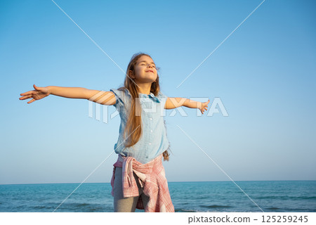 Little girl relaxing and smiling on the beach against blue sea. 125259245