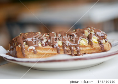 Delicious eclair topped with chocolate and nuts on a plate 125259550
