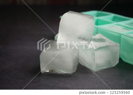 Ice cubes resting beside an ice tray on a dark surface Ice cubes resting beside an ice tray on a dark surface 125259560