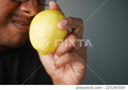 Man examining a yellow lemon in a close-up setting indoors Man examining a yellow lemon in a close-up setting indoors 125260389